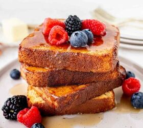 air fryer french toast easy ready in minutes, A stack of three thick slices of French toast topped with syrup fresh raspberries blueberries and a blackberry served on a light colored plate with extra berries around the toast
