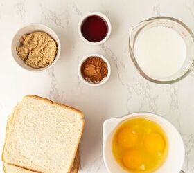 air fryer french toast easy ready in minutes, A flat lay of ingredients on a white marble surface three slices of white bread a bowl with three eggs a measuring cup of milk and small bowls of brown sugar vanilla extract and cinnamon