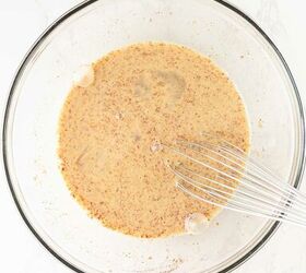 air fryer french toast easy ready in minutes, A glass mixing bowl filled with a light brown speckled liquid mixture and a metal whisk resting inside on a white marble surface