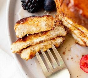 air fryer french toast easy ready in minutes, A close up of a fork holding a cut piece of French toast on a plate with syrup drizzled on top and fresh blackberries blueberries and a raspberry beside it