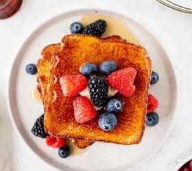 air fryer french toast easy ready in minutes, Two slices of French toast topped with fresh raspberries blueberries and blackberries drizzled with syrup served on a white plate Butter syrup and extra berries are visible around the plate