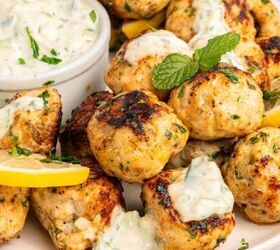 greek beef meatballs in tomato sauce soutzoukakia, A plate of Greek chicken meatballs garnished with lemon slices and herbs served with a small bowl of creamy dipping sauce topped with chopped parsley