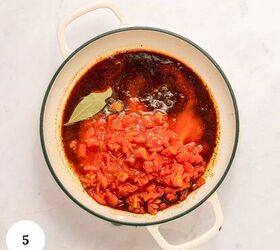 greek beef meatballs in tomato sauce soutzoukakia, A white pot with handles contains diced tomatoes a bay leaf and spices simmering in a rich Soutzoukakia tomato sauce The number 5 is displayed in a white circle in the lower left corner The pot rests on a light marble surface