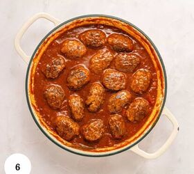 greek beef meatballs in tomato sauce soutzoukakia, A round white pot filled with Greek Beef Meatballs or Soutzoukakia simmering in a rich red tomato sauce viewed from above There is a white circle with the number 6 in the lower left corner