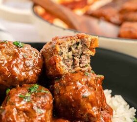 greek beef meatballs in tomato sauce soutzoukakia, Three Greek beef meatballs or Soutzoukakia in a rich tomato sauce sit atop white rice in a black bowl One meatball is cut open revealing a moist herbed interior Fresh herbs are sprinkled on top with more meatballs in the background