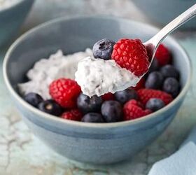easy high protein greek yogurt bowl with chia seeds berries, A low angle side shot of a high protein Greek yogurt bowl filled with fresh berries A spoon has taken a scoop out It is filled with creamy yogurt and chia seeds and has a raspberry and blueberry too