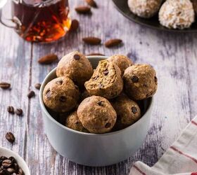 protein balls recipe 3 delicious flavor variations, A small baby blue bowl filled with almond espresso protein balls The top one has a bite out of it All balls contain chocolate chips In the background is a small jar of maple syrup and plate filled with coconut protein balls
