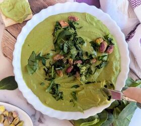 black garlic vegan pesto, A bowl of thick creamy green hummus garnished with chopped fresh spinach and whole pistachios served on a wooden board with spinach leaves gluten free crackers and a small dish of herbs on the side A patterned towel adds a cozy touch