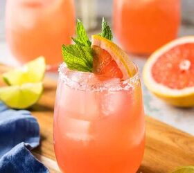 paloma cocktail recipe, A low angle 45 shot of a non stemmed wine glass filled with a pink paloma cocktail In the background are two more palomas All are garnished with a grapefruit wedge and a sprig of mint in the glass