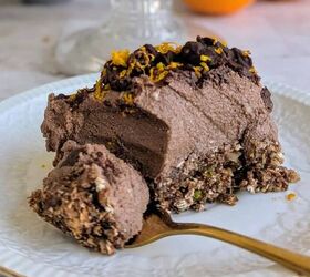 crunchy chocolate puffed rice easter cups 4 ingredients, A slice of no bake chocolate orange mousse cake on a white plate with a creamy chocolate filling crunchy nutty oat base and topped with chocolate chunks and grated orand rind The whole cake is displayed on a glass stand in the background with fresh oranges