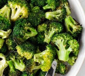 air fryer broccoli, A close up of roasted broccoli florets in a white bowl with a wooden handled serving utensil The broccoli is slightly browned indicating it has been roasted