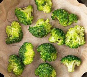 air fryer broccoli, Fresh broccoli florets arranged on a sheet of parchment paper inside a black round air fryer basket ready to be cooked
