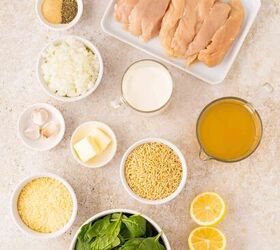 lemon chicken orzo pasta one pan, Overhead view of raw chicken breasts olive oil chopped onions garlic cloves spices butter cream chicken broth uncooked orzo grated Parmesan fresh spinach and halved lemons on a light countertop