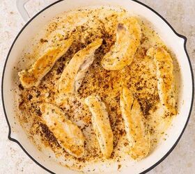 lemon chicken orzo pasta one pan, Seven cooked chicken tenders are arranged in a white skillet with browned seasoning and pan drippings visible The skillet sits on a light colored surface