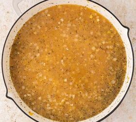 lemon chicken orzo pasta one pan, A large white pot filled with a light brown broth and orzo containing visible chopped onions and herbs sitting on a light colored countertop