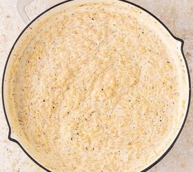 lemon chicken orzo pasta one pan, A large shallow pan filled with creamy cooked orzo pasta in a white sauce with visible herbs sitting on a light colored countertop