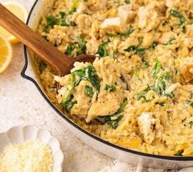 lemon chicken orzo pasta one pan, A skillet filled with creamy orzo pasta chunks of chicken spinach and grated cheese a wooden spoon scoops some up Sliced lemons and a small bowl of grated cheese are nearby