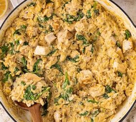 lemon chicken orzo pasta one pan, A large white skillet filled with creamy orzo pasta pieces of cooked chicken and fresh spinach A wooden spoon is scooping up a portion Slices of lemon and a plate are visible nearby