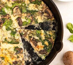 easy egg white frittata fluffy high protein, A skillet filled with a sliced mushroom and spinach egg white frittata One wedge is being removed and fresh mushrooms and spinach leaves are scattered nearby on a white surface Plates and a fork are in the background