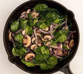 easy egg white frittata fluffy high protein, A black skillet filled with saut ed spinach sliced mushrooms and red onions on a light colored surface