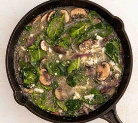 easy egg white frittata fluffy high protein, A black skillet filled with a mixture of spinach leaves sliced mushrooms onions and egg whites on a light colored surface