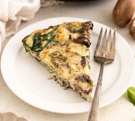 easy egg white frittata fluffy high protein, A slice of egg white frittata with mushrooms spinach and herbs is served on a white plate with a fork Fresh spinach leaves and mushrooms are visible nearby on the light colored table