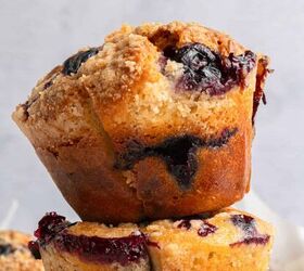 blueberry yogurt muffins with crumble topping, A close up of golden brown blueberry yogurt muffins with a crumbly topping and visible blueberry filling stacked on top of each other against a light background