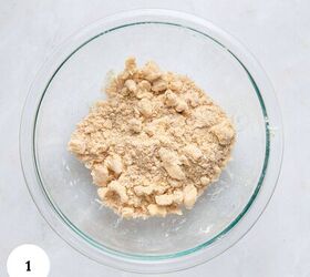 blueberry yogurt muffins with crumble topping, A clear glass bowl filled with crumbly dough mixture for blueberry yogurt muffins sits on a white marble surface A white circle with the number 1 is in the bottom left corner of the image