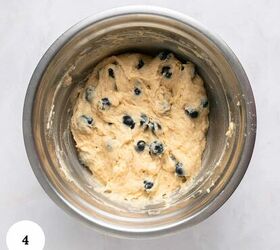 blueberry yogurt muffins with crumble topping, A stainless steel mixing bowl holds a thick creamy batter dotted with blueberries for blueberry yogurt muffins The bowl sits on a light marble surface and a white circle with the number 4 appears in the lower left corner