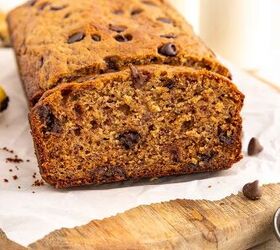 chocolate chip banana bread ultra moist easy, A loaf of chocolate chip banana bread sits on parchment paper atop a wooden board with one slice cut to show its moist texture and chocolate chips inside There are chocolate chips and a banana nearby