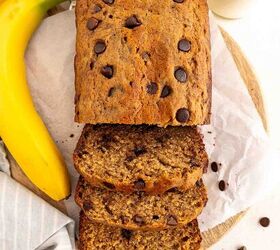 chocolate chip banana bread ultra moist easy, A loaf of chocolate chip banana bread partially sliced sits on parchment paper with whole bananas scattered chocolate chips and two glasses of milk nearby on a light surface