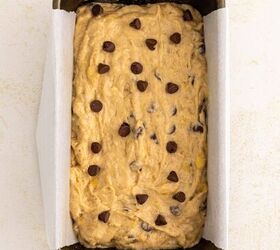 chocolate chip banana bread ultra moist easy, A loaf pan lined with parchment paper filled with unbaked banana bread batter topped with chocolate chips sits on a light colored surface