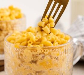 microwave mac and cheese, A fork lifts a portion of creamy macaroni and cheese from a decorative glass mug filled with pasta Another cup of mac and cheese and a milk bottle are blurred in the background