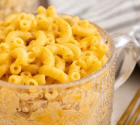 microwave mac and cheese, A clear patterned glass cup filled with creamy macaroni and cheese sits on a table beside a gold fork and a striped cloth napkin