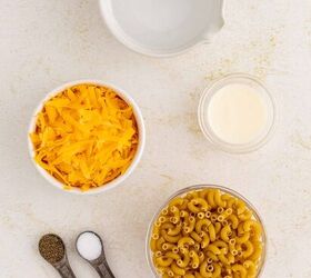 microwave mac and cheese, A flat lay of mac and cheese ingredients a bowl of shredded cheddar cheese uncooked elbow macaroni a small bowl of cream a bowl of water and two measuring spoons with salt and pepper
