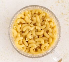 microwave mac and cheese, A clear glass mug filled with cooked elbow macaroni and creamy cheese sauce sits on a light textured surface