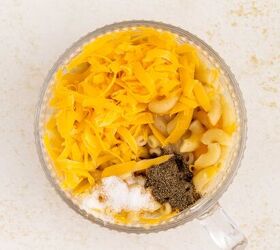 microwave mac and cheese, A clear glass mug filled with cooked macaroni shredded cheddar cheese ground black pepper and salt on a light speckled surface