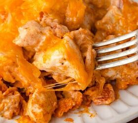 doritos casserole, Close up of a cheesy chicken casserole on a white plate A fork is lifting a piece revealing layers of melted cheese and chunks of chicken mixed with a creamy sauce The dish has a golden brown crust