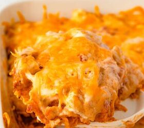 doritos casserole, A close up of a cheesy tortilla chip casserole in a white baking dish A slice is being lifted revealing layers of melted cheese and crunchy chips The background has an orange napkin and another part of the dish visible