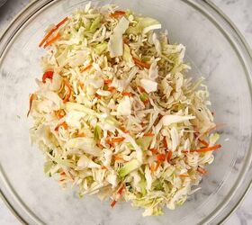 creamy coleslaw with celery seed, A clear glass bowl filled with shredded cabbage carrots and other vegetables sits on a marble surface A gray cloth is partially visible in the top left corner