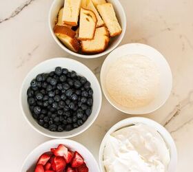 easy no bake parfait cups with fresh berries, Ingredients for parfait cups including sliced strawberries blueberries vanilla pudding whipped topping and pound cake arranged in white bowls on a marble countertop