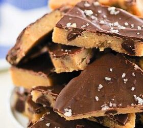 easy no bake cookie dough bark edible safe to eat, A plate stacked with pieces of chocolate covered cookie dough topped with flaky sea salt The dough has a golden base and a thick chocolate layer set against a blurred blue and white background
