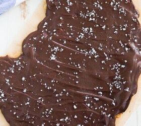 easy no bake cookie dough bark edible safe to eat, A large slab of cookie dough in a smooth layer of chocolate and sprinkled with sea salt sits on parchment paper A blue and white checkered cloth and a small jar of cookies are visible in the background