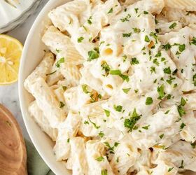 lemon ricotta pasta without heavy cream, A bowl of rigatoni pasta covered in creamy white sauce garnished with chopped parsley A wooden spoon lemon half and forks are nearby on a marble surface