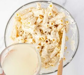 lemon ricotta pasta without heavy cream, A glass bowl filled with cooked rigatoni pasta coated in a creamy white sauce sits on a marble surface A hand is pouring a cup of starchy pasta water into the bowl and a spatula rests inside