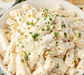lemon ricotta pasta without heavy cream, A bowl of rigatoni pasta coated in a creamy white sauce and garnished with chopped parsley with breadsticks and lemon in the background