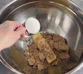edible peanut butter cookie dough no eggs no bake, A hand holds a measuring spoon of white sugar over a metal bowl containing sticks of butter and piles of brown sugar ready to be mixed The bowl is set on a gray countertop