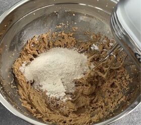 edible peanut butter cookie dough no eggs no bake, A metal mixing bowl with brown cookie dough and flour being mixed with a handheld electric mixer on a gray countertop