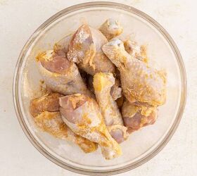 air fryer chicken legs crispy juicy and easy, Raw chicken drumsticks coated in seasoning are arranged in a clear glass bowl on a light textured surface