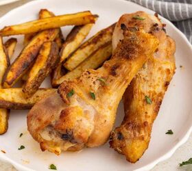 air fryer chicken legs crispy juicy and easy, Two seasoned and chicken drumsticks served on a white plate with crispy potato wedges A small bowl of sauce and fresh parsley leaves are visible nearby with a gray striped napkin in the background